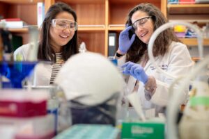 Two women in white coats in a lab surrounded by scientific equipment